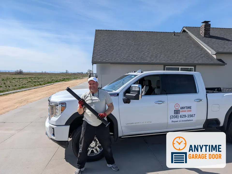 Man in an Anytime Garage Door cap holding a long torsion spring in front of a white company pickup truck
